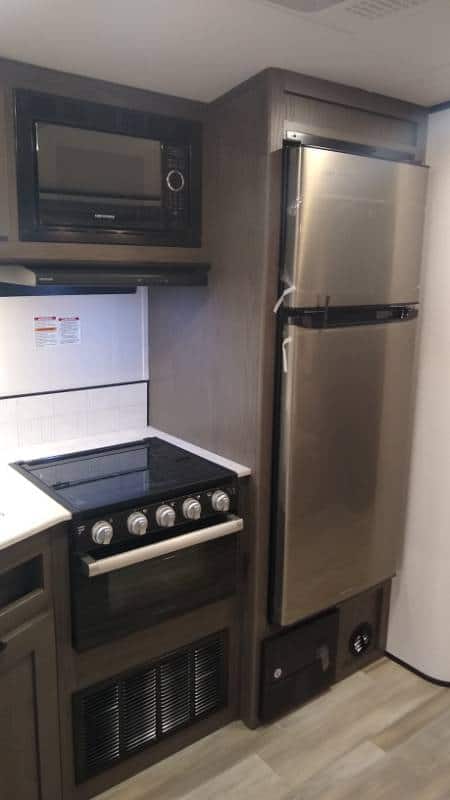 RV kitchen with refrigerator and black painted range hood above glass-top stove