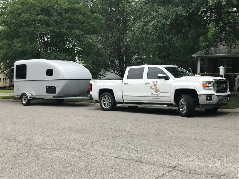 A tiny fiberglass camper being towed by a small truck