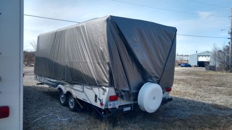 Old RV in storage beneath large gray tarp
