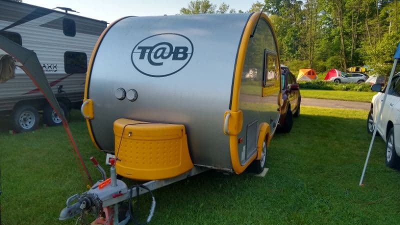 NuCamp travel trailer with yellow trim camping on grass