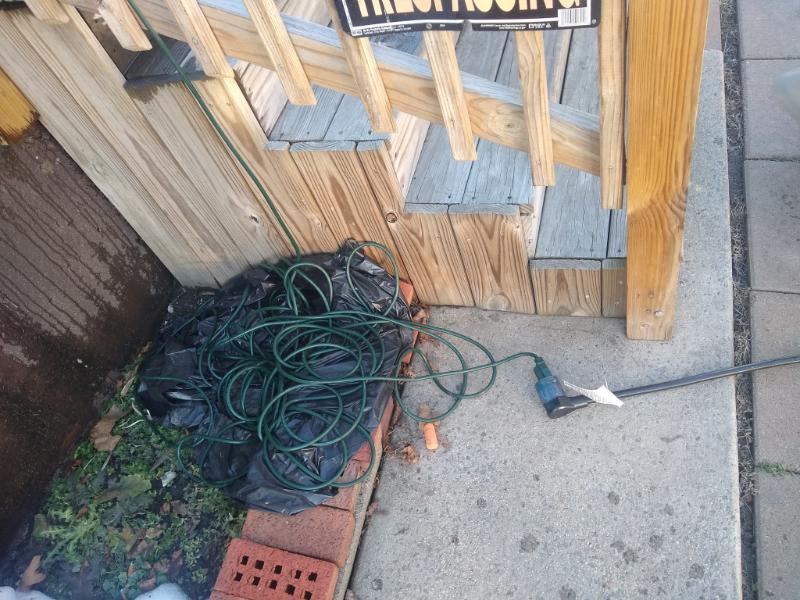 A long, green residential extension cord coiled on the ground outside.